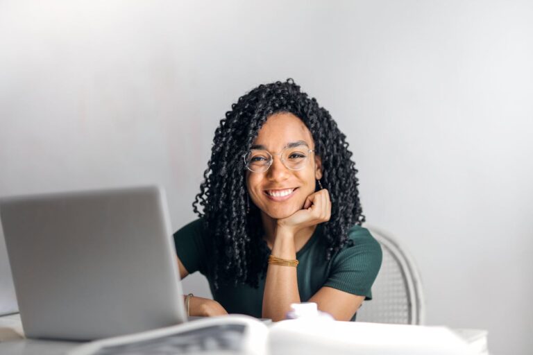 a young woman with dreadlocks smiling while sitting at a desk with a laptop